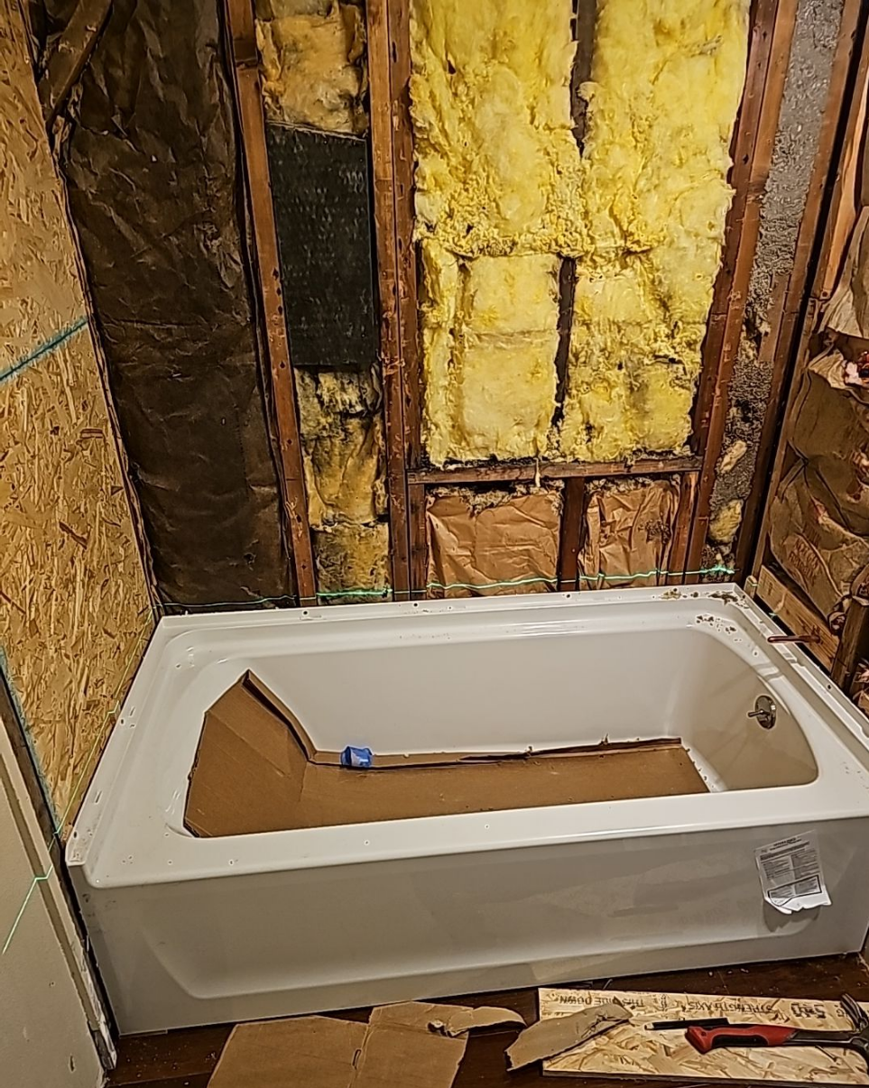 Bathroom renovation showing early stages with exposed walls and tub installation